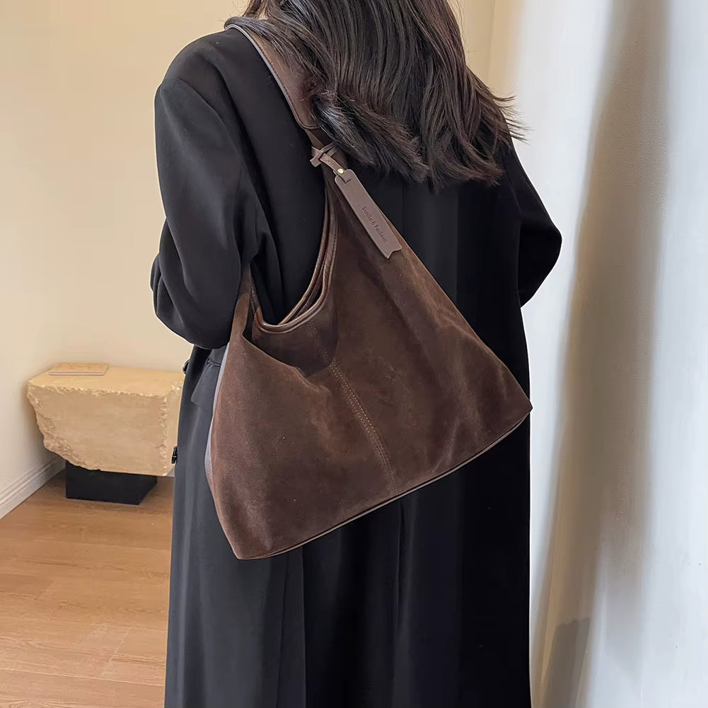 Woman styling a chic brown suede bag, effortlessly complementing her outfit with a timeless and elegant accessory – available at Shop Style Edit.