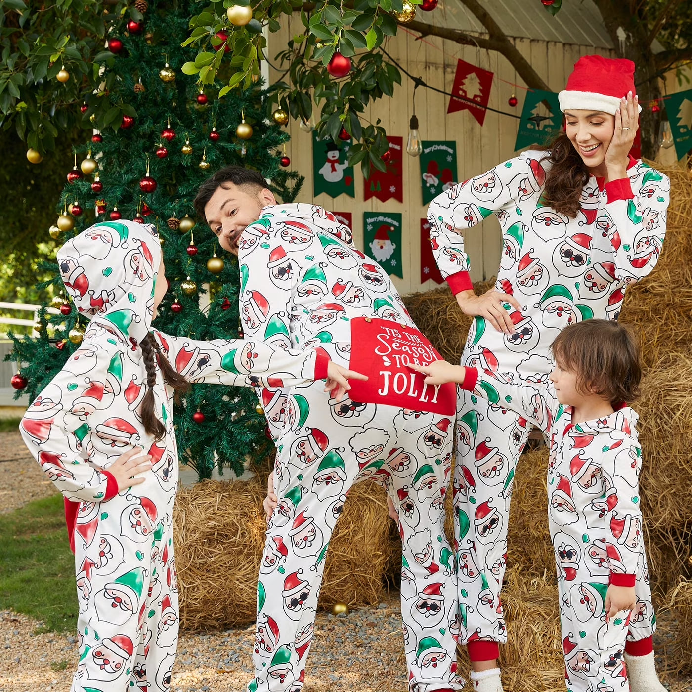 Family in matching Christmas-themed pajamas outdoors with holiday decorations.