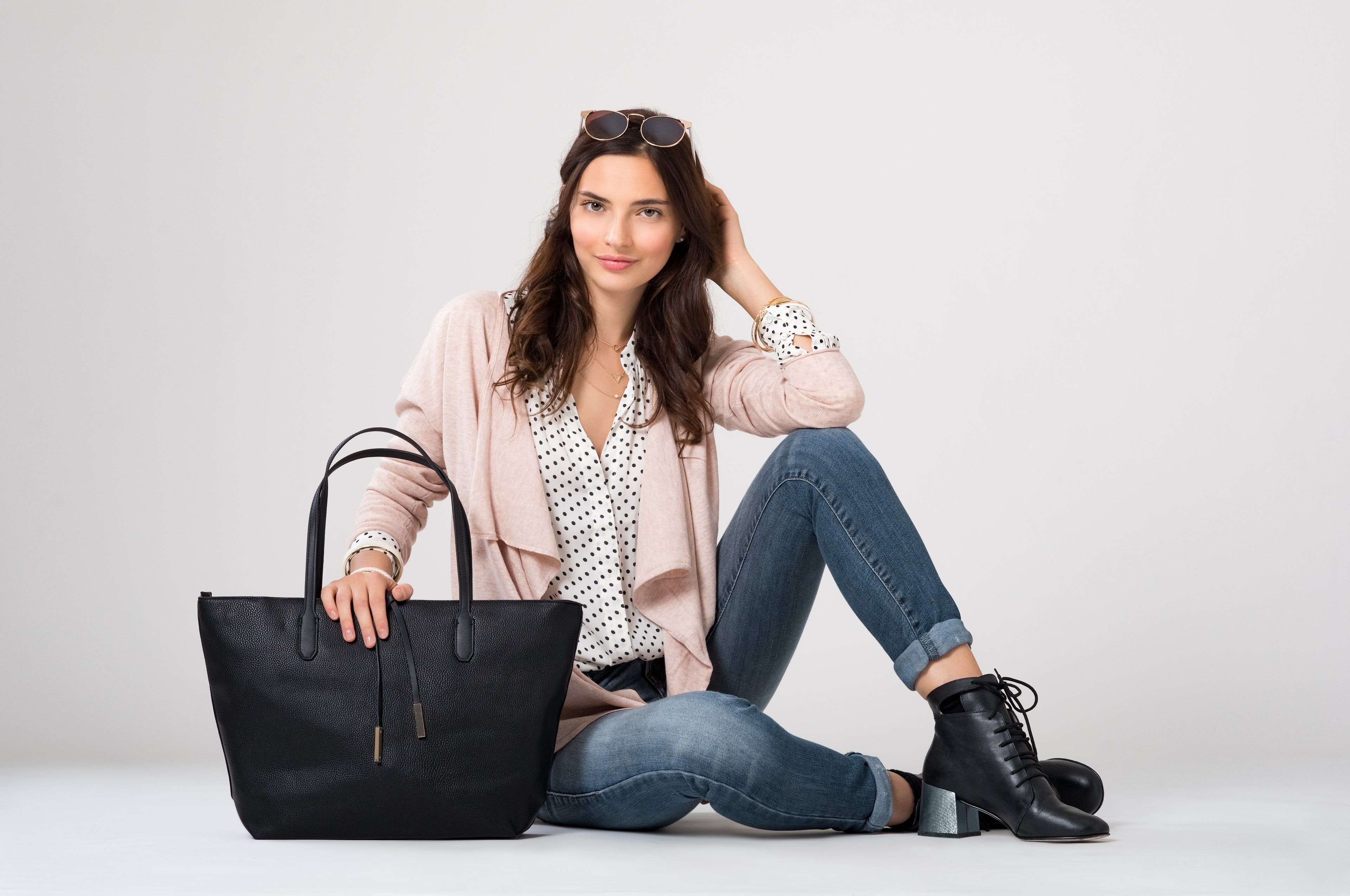 Portrait of a woman indoors in a studio, wearing a stylish white and black polka dot top paired with a chic jacket and classic jeans – a perfect blend of casual and trendy fashion from Shop Style Edit.