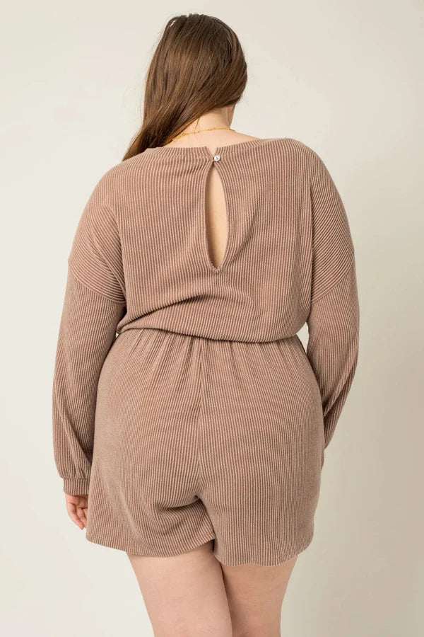 Back view of a plus size model wearing a mocha ribbed long sleeve romper featuring a keyhole back and drawstring waist.