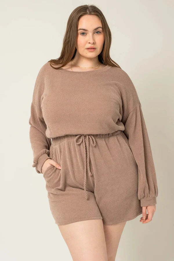 Plus size model wearing a mocha ribbed long sleeve drawstring romper with pockets, front view on a neutral background.